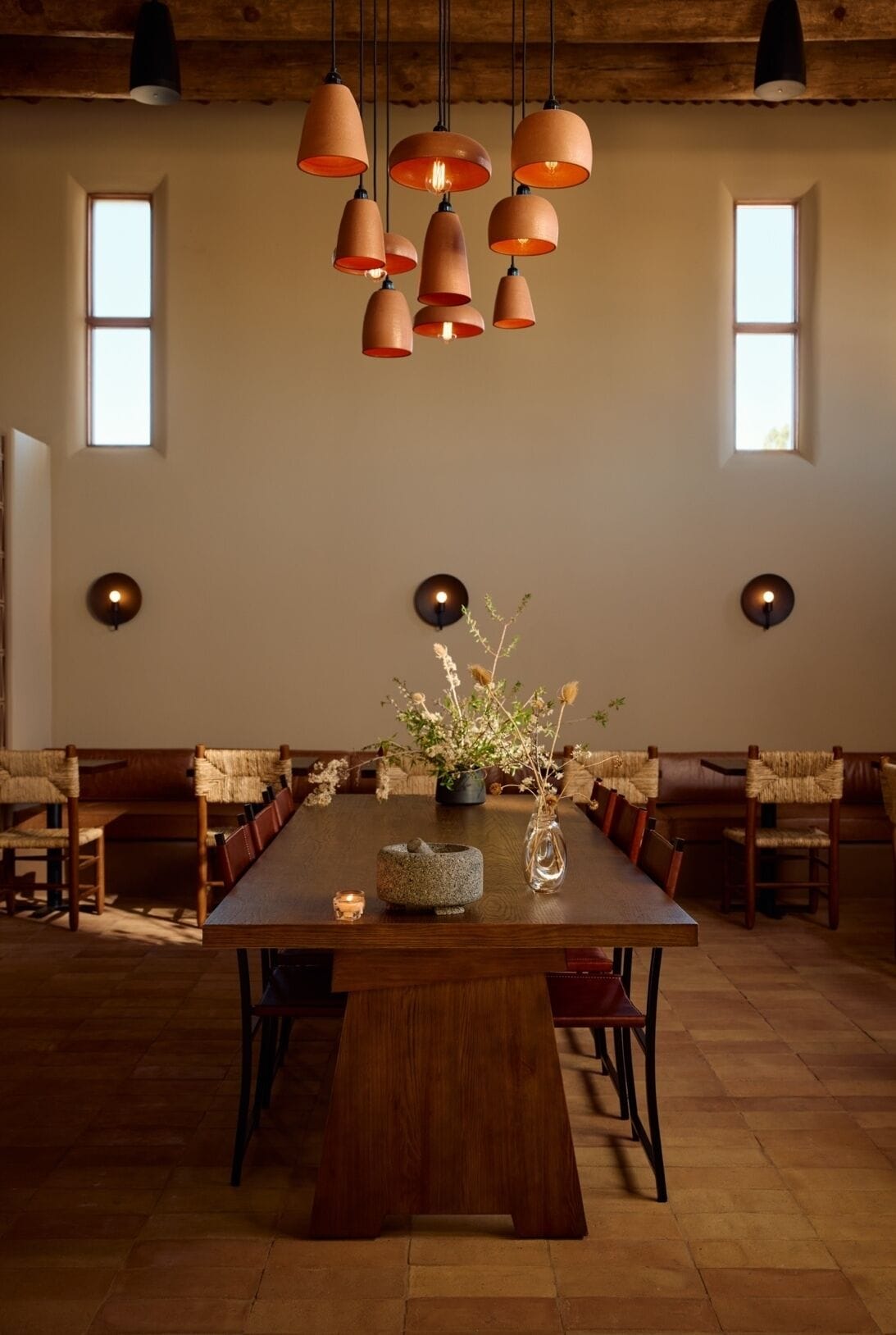 A dining area with a wooden table, chairs, hanging terracotta lamps, and wall sconces.