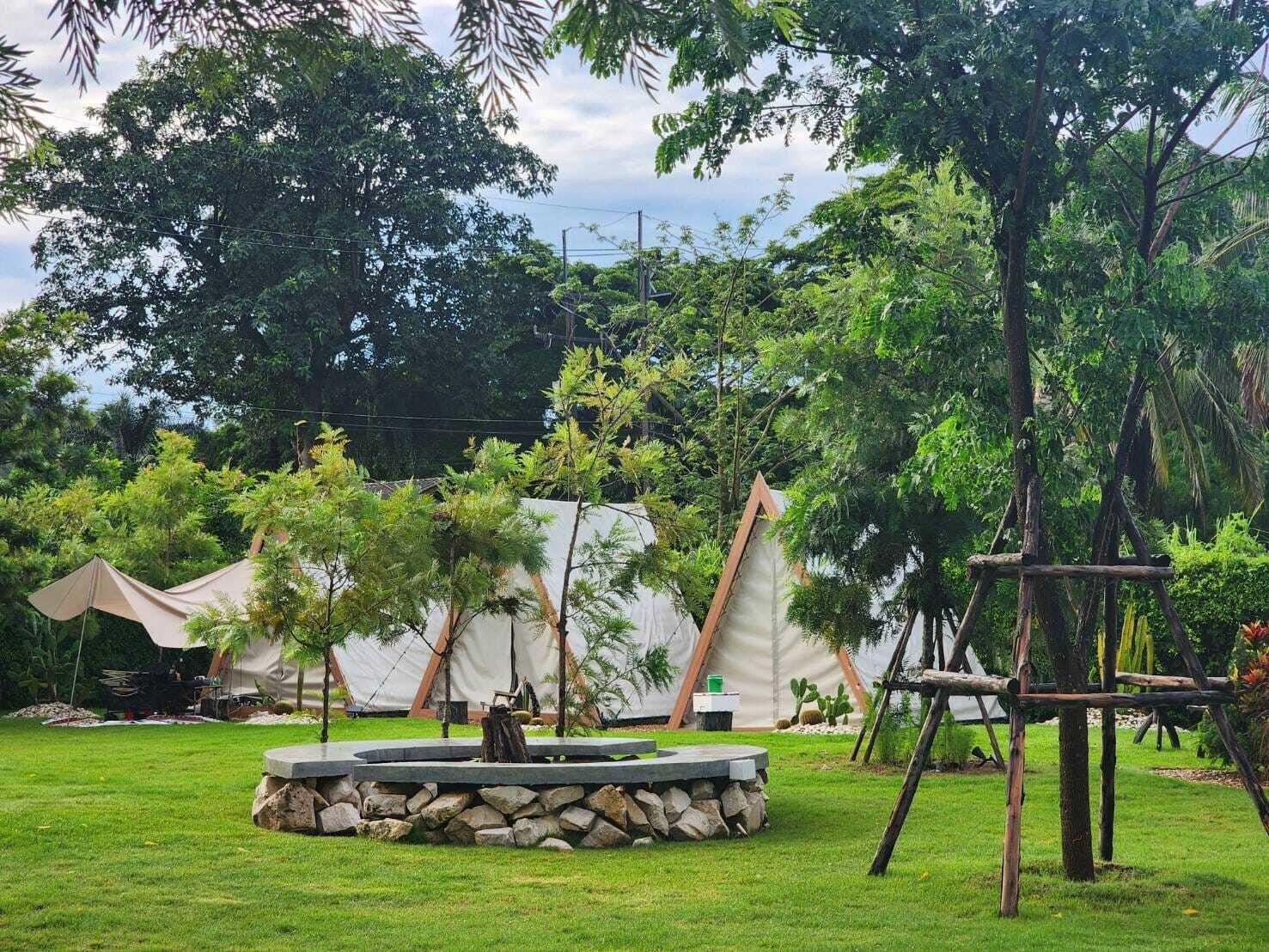 Un terrain de camping avec des tentes, une structure centrale en pierre et des arbres tout autour.