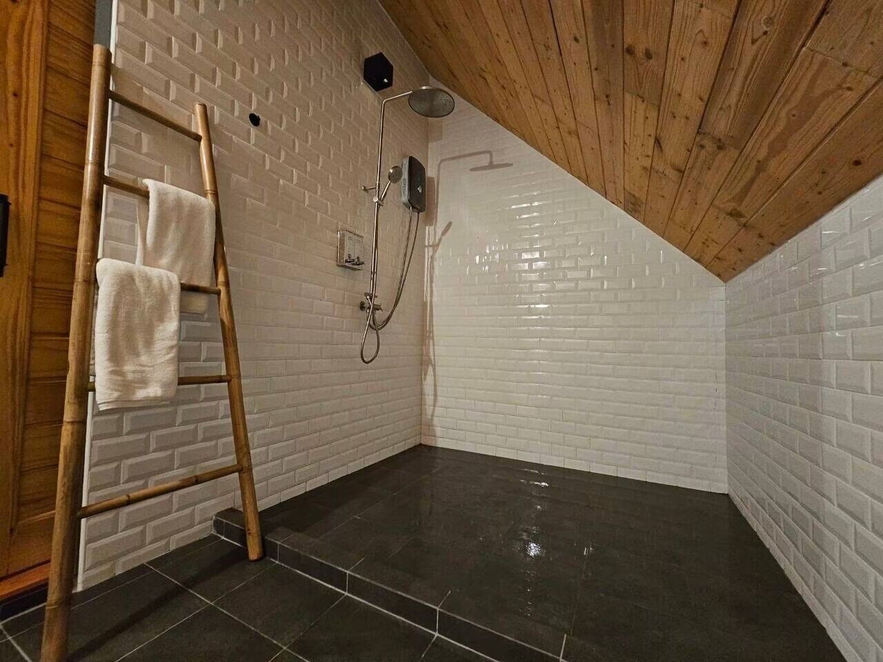Un baño pequeño con techo inclinado, paredes de ladrillo blanco y baldosas oscuras.
