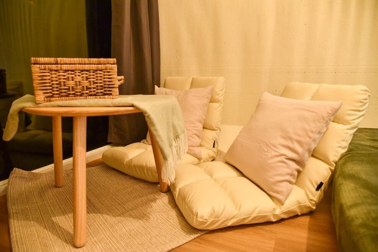 A cozy living room with a woven basket on a small wooden table, a beige sofa with cushions, and a green couch.