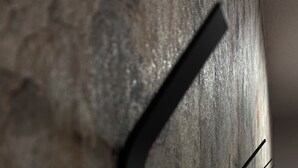 Primer plano de una pared texturizada con un soporte metálico negro y angular.