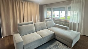 Una sala de estar moderna con un sofá seccional, un ventanal con persianas y una lámpara de techo.