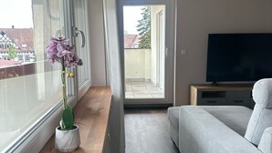 Un dormitorio moderno con sofá, televisor y ventana con vista a edificios.