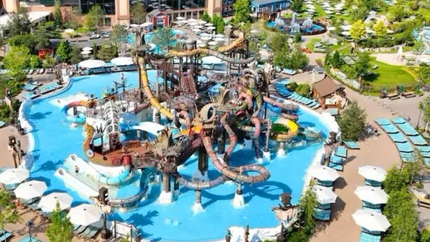 Parque acuático con una piscina grande, toboganes y un edificio al fondo.