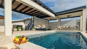 A modern outdoor pool area with a clear pool, lounge chairs, and a fruit bowl on the edge.