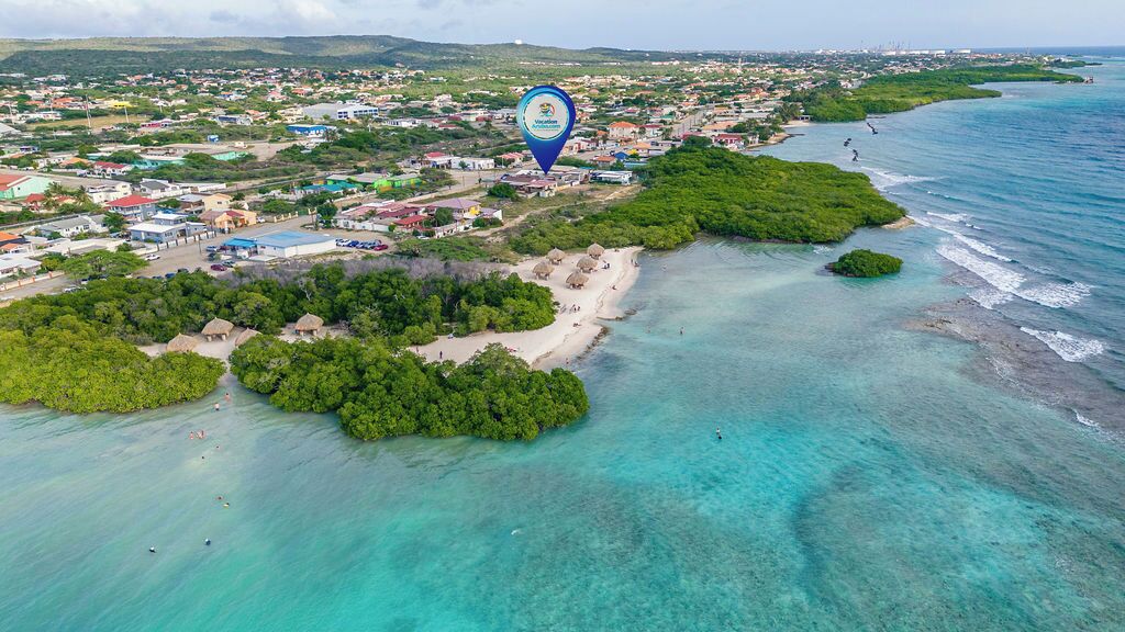 Vista aérea de un pueblo costero con playa, aguas turquesas cristalinas y abundante vegetación.