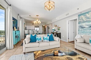 A modern living room with a sofa, coffee table, and a painting of the ocean. - 3b3ba | Gulf Front | Pool, Hot Tub | Beach Chairs! (Panama City Beach)