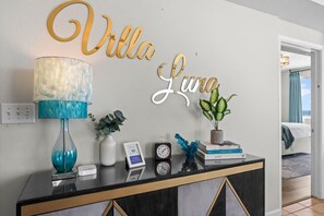 A reception desk with a lamp, a potted plant, a clock, and a sign that reads 'Villa Luna.' - 3b3ba | Gulf Front | Pool, Hot Tub | Beach Chairs! (Panama City Beach)