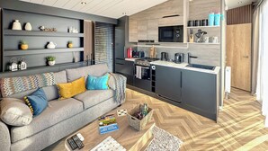 A modern kitchen with built-in appliances, a grey sofa with colorful cushions, and a wooden herringbone floor. - 1 bedroom accommodation in Sandgreen (Sandgreen)