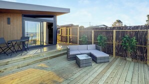 A wooden deck with outdoor furniture, a sliding glass door, and a bamboo fence. - 1 bedroom accommodation in Sandgreen (Sandgreen)