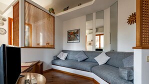 A modern living room with a grey sofa, wooden flooring, a TV, and a decorative screen. - GuestHost - Cozy 2-Bedroom Stay at Lido di Venezia (Lido)