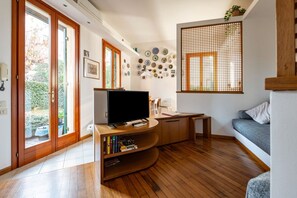 A modern living room with a flat-screen TV, wooden flooring, a bookshelf, a sofa, and a wall decorated with plates.