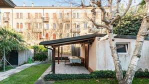 A covered outdoor seating area with a table and chairs, surrounded by a garden and a building with balconies. - GuestHost - Cozy 2-Bedroom Stay at Lido di Venezia (Lido)