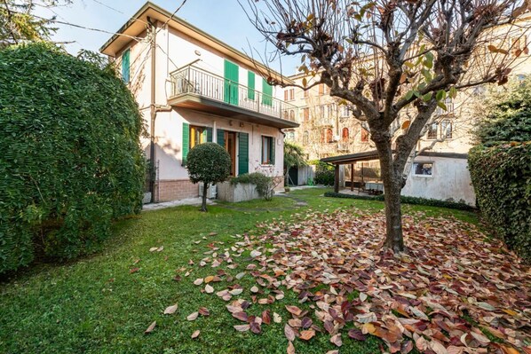 A residential building with a balcony, a lawn, and a tree with fallen leaves.