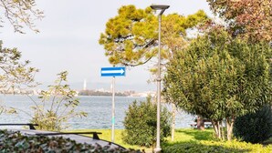 A park with a directional sign, a lamp post, and a body of water in the background. - GuestHost - Cozy 2-Bedroom Stay at Lido di Venezia (Lido)