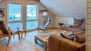 Un salon chaleureux de style industriel, avec une grande fenêtre, un plancher en bois, un canapé en cuir marron, une table basse en bois et un fauteuil bleu.
