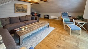 Un salon confortable avec un canapé, une table basse et un fauteuil. Il y a un tableau au mur et une petite table avec des livres.