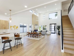 Amplia sala de estar con suelo de madera, una mesa de comedor con sillas, un sofá, un televisor y una escalera.