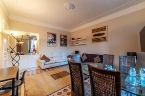 A living room with a sofa, dining table, chairs, and a kitchen area in the background.