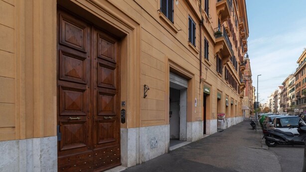 Un edificio con ampie porte in legno, una strada stretta, auto parcheggiate e altri edifici.