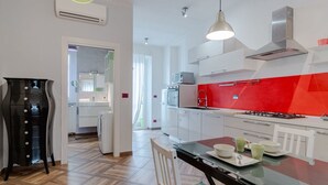 Una cucina moderna con mobili bianchi, uno schienale rosso e un'area pranzo con un tavolo e sedie in vetro.