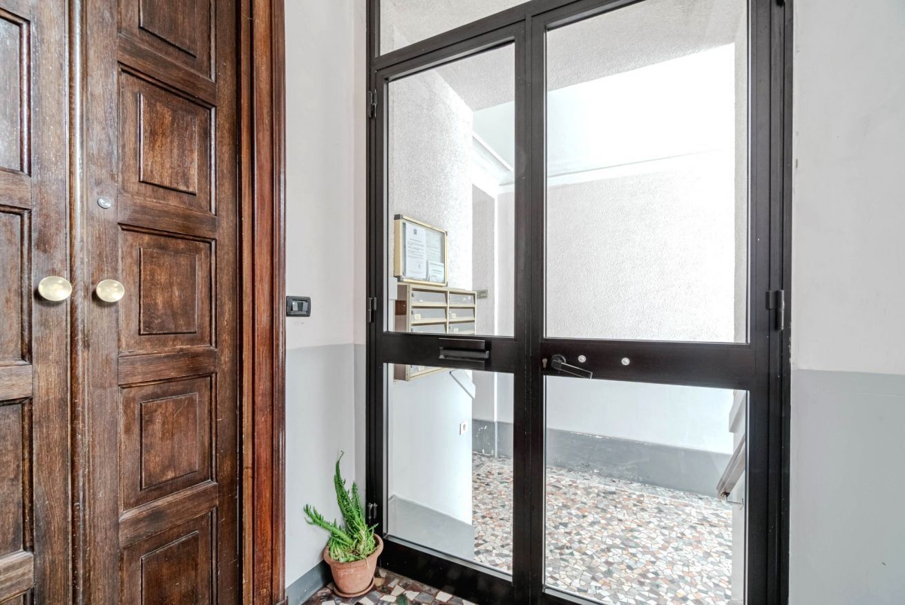 A wooden door with a glass panel, a potted plant, and a glimpse of a tiled courtyard.