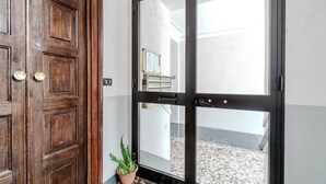 Una porta in legno con un vetro, un vaso con una pianta e uno scorcio di un cortile piastrellato.