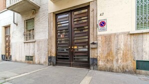 Un edificio con un'ampia porta doppia marrone scuro, un segnale di divieto di sosta e una piccola finestra con una griglia metallica.