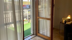 Une pièce dotée d’une porte-fenêtre coulissante donnant sur un balcon, qui offre une vue sur une cour clôturée et un bâtiment situé au loin.