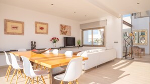 A modern living room with a wooden dining table, white chairs, a sofa, and a TV. - VILLA MONTFARRUTX - Modern villa with private swimming pool and free Wifi (Artà)