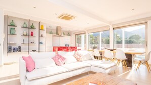 A modern living room with a white sectional sofa, a wooden coffee table, and a dining area with white chairs and a red table. - VILLA MONTFARRUTX - Modern villa with private swimming pool and free Wifi (Artà)