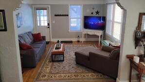 Un salon avec un canapé gris, un canapé marron, une table basse, un téléviseur et un tapis à motifs.