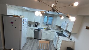 A modern kitchen with white cabinets, a stainless steel refrigerator, a dining table with chairs, and a ceiling light fixture.