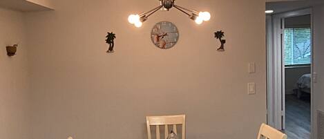 A dining area with a round table, four chairs, a chandelier, and a wall clock.