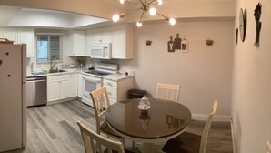 A compact kitchen with white cabinets, a refrigerator, a microwave, and a stove. There is a dining table with chairs and a chandelier.