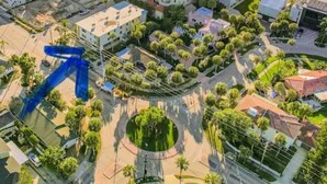 An aerial view of a coastal residential area with buildings, a large blue arrow sculpture, and a beach in the background.