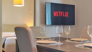 Une chambre d’hôtel comprenant un coin repas, un lit et un téléviseur affichant le logo de Netflix.
