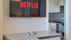 Une cuisine moderne équipée d’un téléviseur à écran plat affichant le logo de Netflix, d’un petit panneau décoratif posé sur le comptoir, et on aperçoit une partie de la salle à manger adjacente.