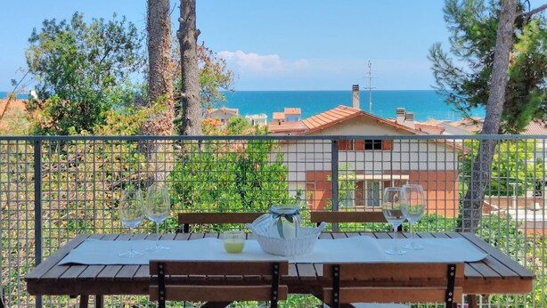 Une table avec deux verres à vin et une bouteille, le tout placé devant un paysage côtier et une maison.