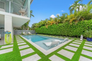 A modern pool area with a clear blue pool, white lounge chairs, and a lush green hedge. - Luxurious 3-bedroom home with Pool and Dock in Key Colony Beach (Key Colony Beach)