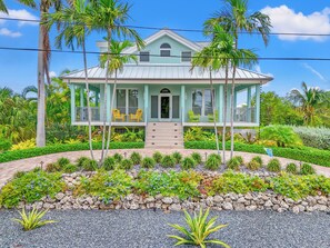 A two-story house with a porch, surrounded by a landscaped garden with various plants and a stone pathway. - Luxurious 3-bedroom home with Pool and Dock in Key Colony Beach (Key Colony Beach)