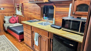 A compact kitchen with wooden cabinetry, a microwave, a sink, and a countertop with a dish soap bottle. - Unique Train Caboose Tiny House & event space. Antique shops & Norman close by  (Lexington)