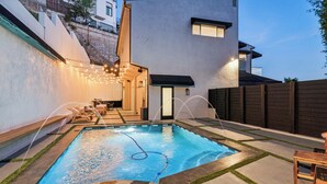A swimming pool with a hot tub, surrounded by a patio with outdoor furniture and string lights. - The Hollywood Hills Luxury Nest with Views, Pool and Spa. (Los Angeles)