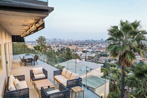 A rooftop terrace with outdoor furniture, a city view, and palm trees.