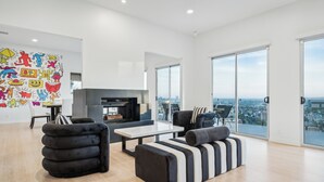 A modern living room with a fireplace, black and white striped sofa, and a colorful mural on the wall. - The Hollywood Hills Luxury Nest with Views, Pool and Spa. (Los Angeles)