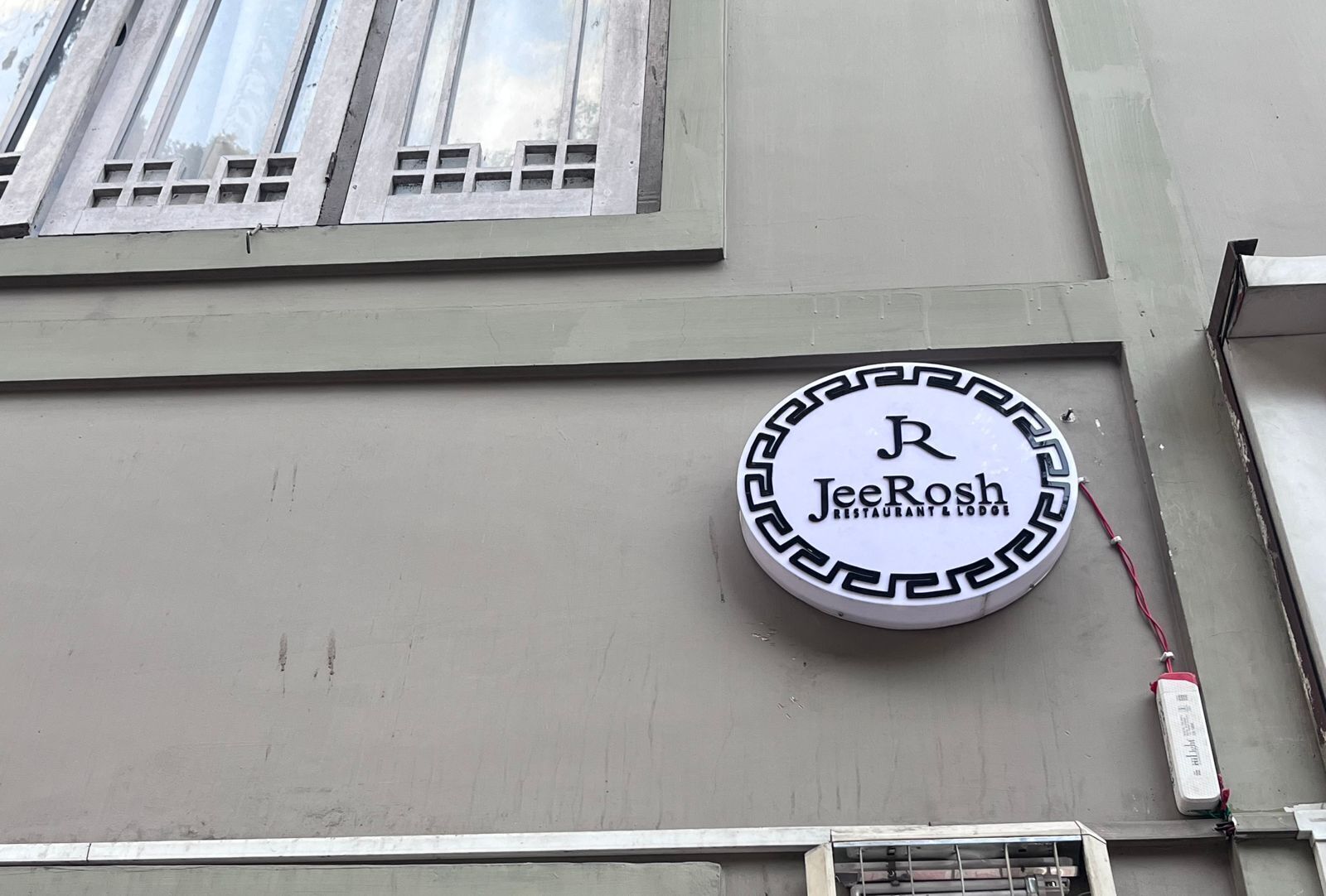 Ein rundes Schild mit dem Schriftzug "JeeRosh Restaurant & Lodge" an einer Gebäudefassade.