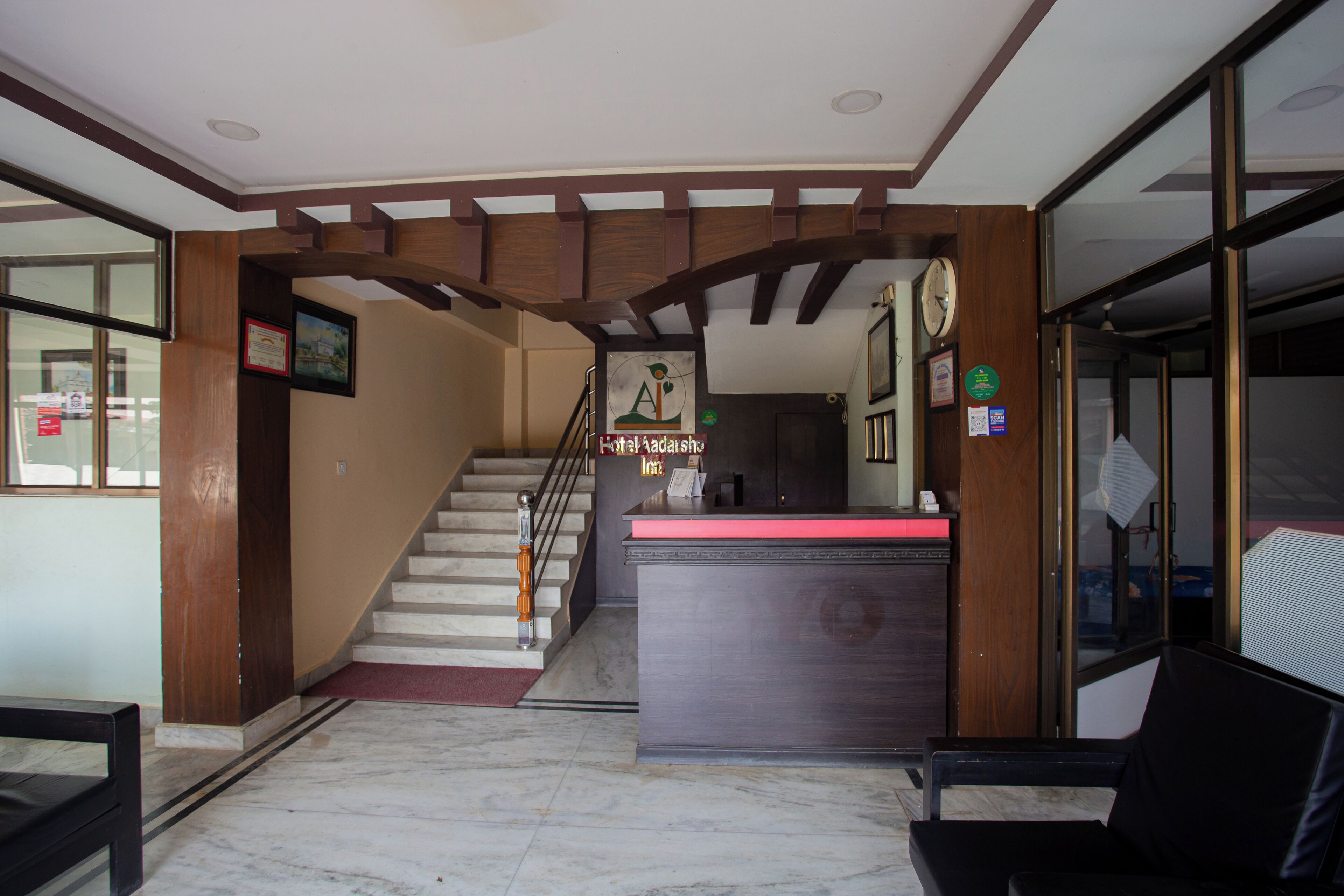 Zona de recepción de hotel con suelo de mármol, mostrador de madera y una escalera que sube a los pisos superiores.