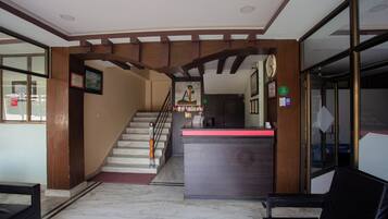 Zona de recepción de hotel con suelo de mármol, mostrador de madera y una escalera que sube a los pisos superiores.