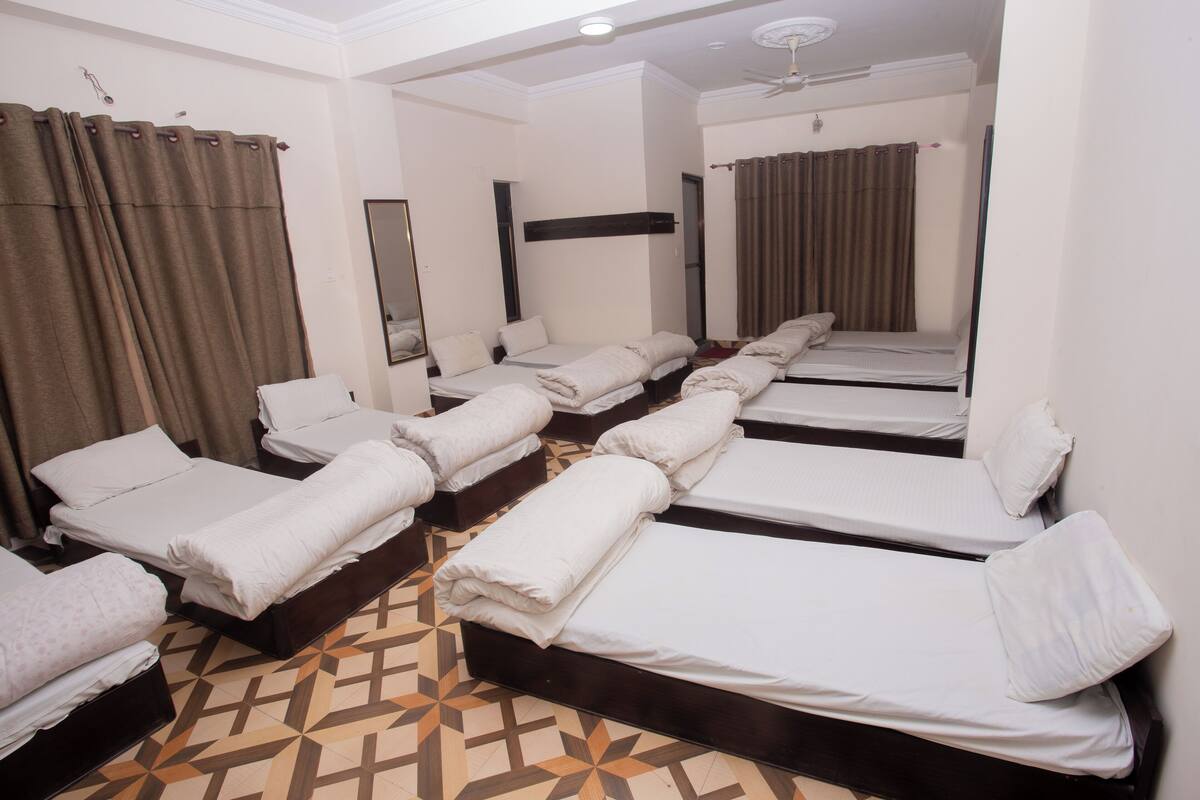A hotel room with multiple single beds arranged in a row, a ceiling fan, and a patterned floor.