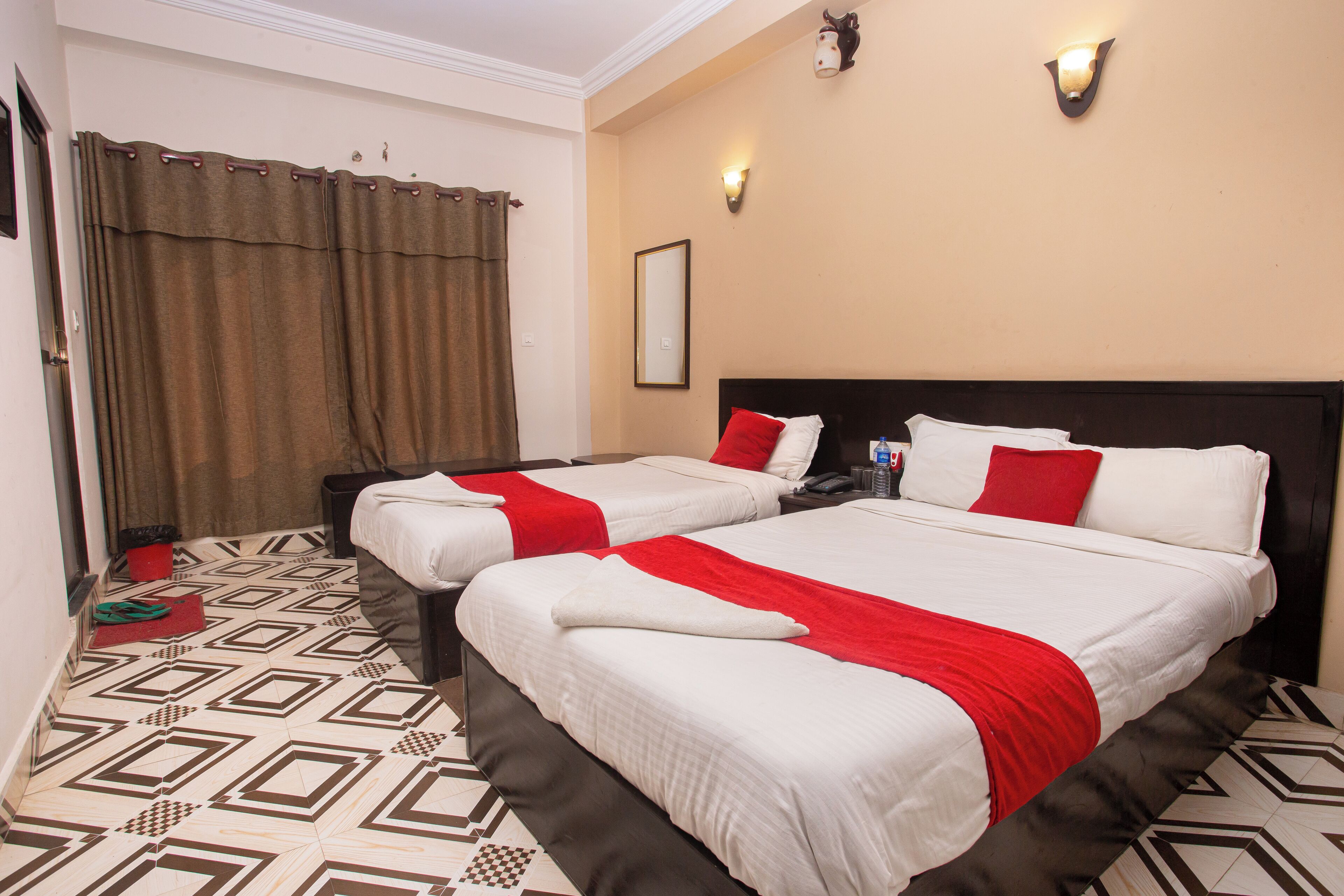 A hotel room with two beds, a patterned floor, and a curtain.